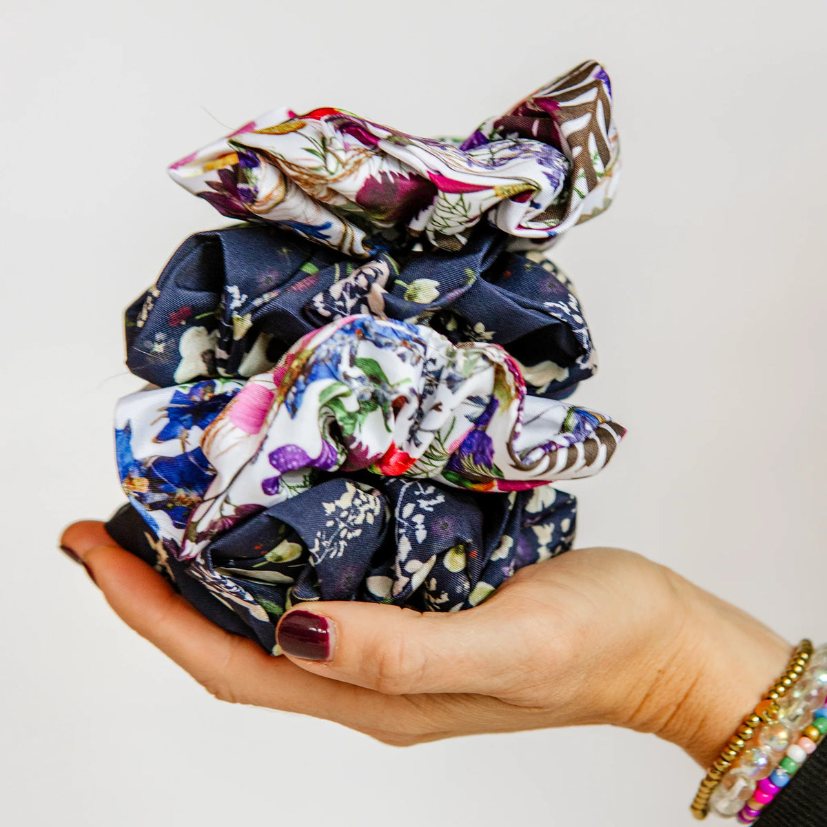 Hand holding a stack of floral scrunchies against a light background