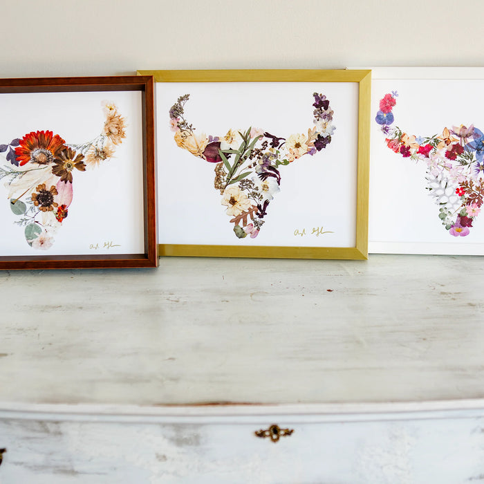 Three framed floral buffalo head art pieces on a wooden surface.