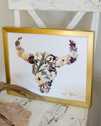 Framed floral buffalo artwork with a gold frame on a textured surface