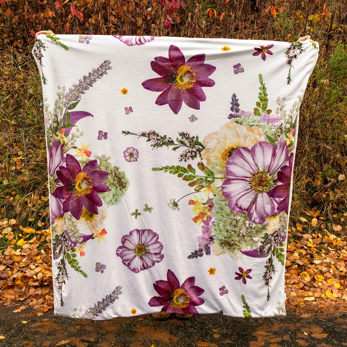 Throw blanket with oversized pressed flowers design being held up in autumn scene outdoors