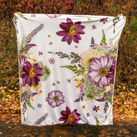 Throw blanket with oversized pressed flowers design being held up in autumn scene outdoors