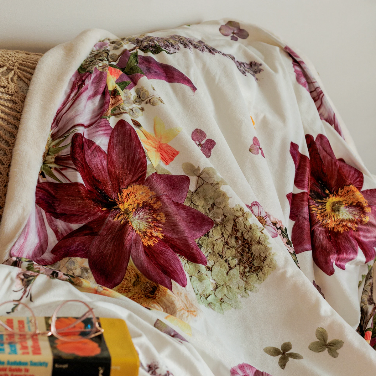 Throw blanket with a pressed flower design on a couch with book and glasses in the foreground