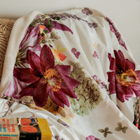 Throw blanket with a pressed flower design on a couch with book and glasses in the foreground