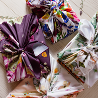 Four presents wrapped in bright reusable fabric gift wrap, knotted at the top and featuring bright floral designs