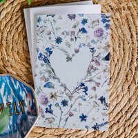 Heart shaped flower card on a woven surface with a colorful object partially visible.