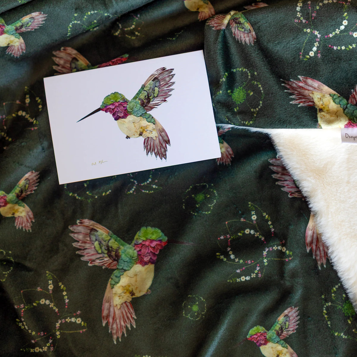 Card with a colorful floral hummingbird on a throw blanket with hummingbird patterns.
