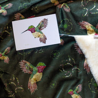 Card with a colorful floral hummingbird on a throw blanket with hummingbird patterns.