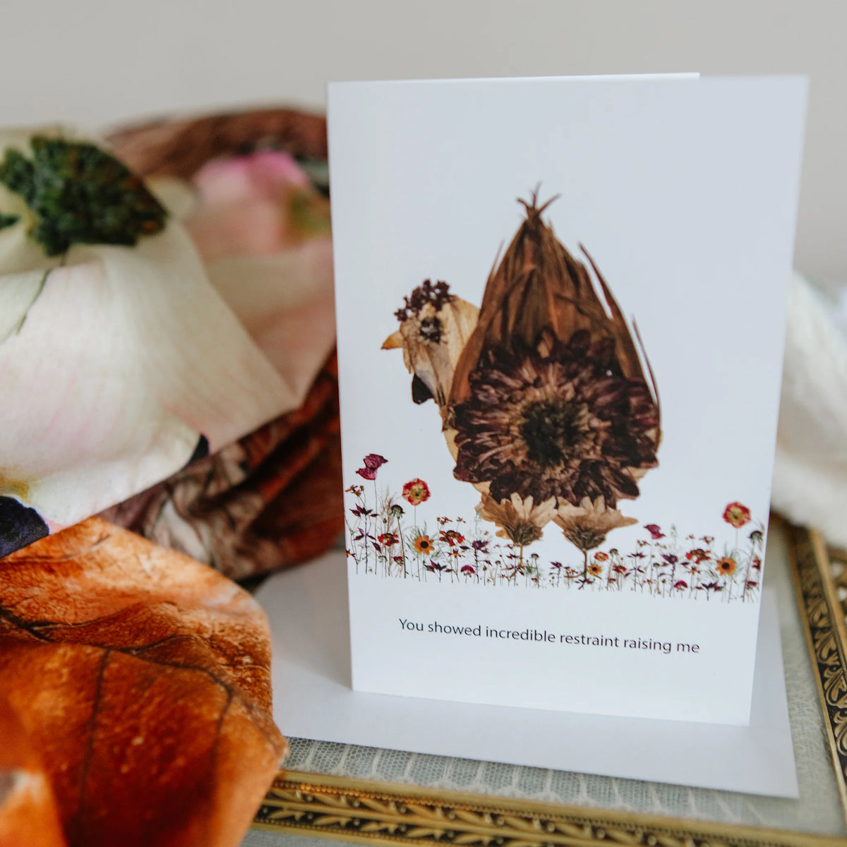 Funny greeting card with a chicken illustration on a surface with flowers and fabric.