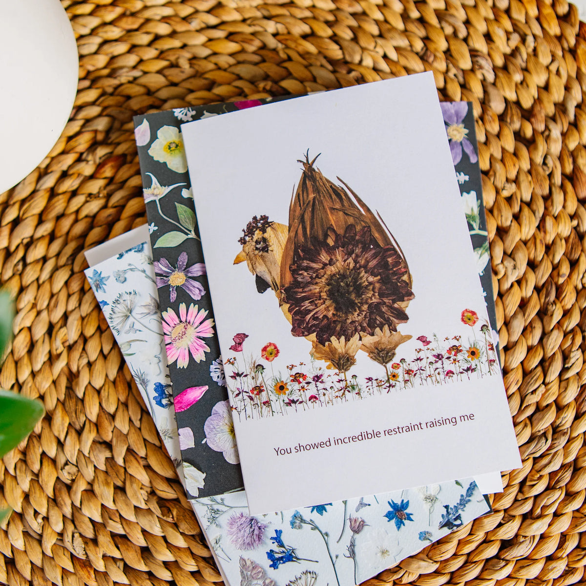 Greeting cards with floral designs and a sunflower chicken theme on a woven surface