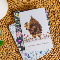 Greeting cards with floral designs and a sunflower chicken theme on a woven surface