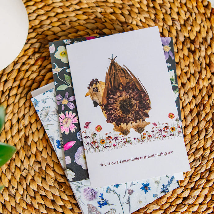 Greeting cards with floral designs and a sunflower chicken theme on a woven surface