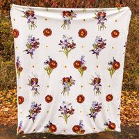 Cream-white blanket with flower cluster design being held up in an autumn setting outdoors