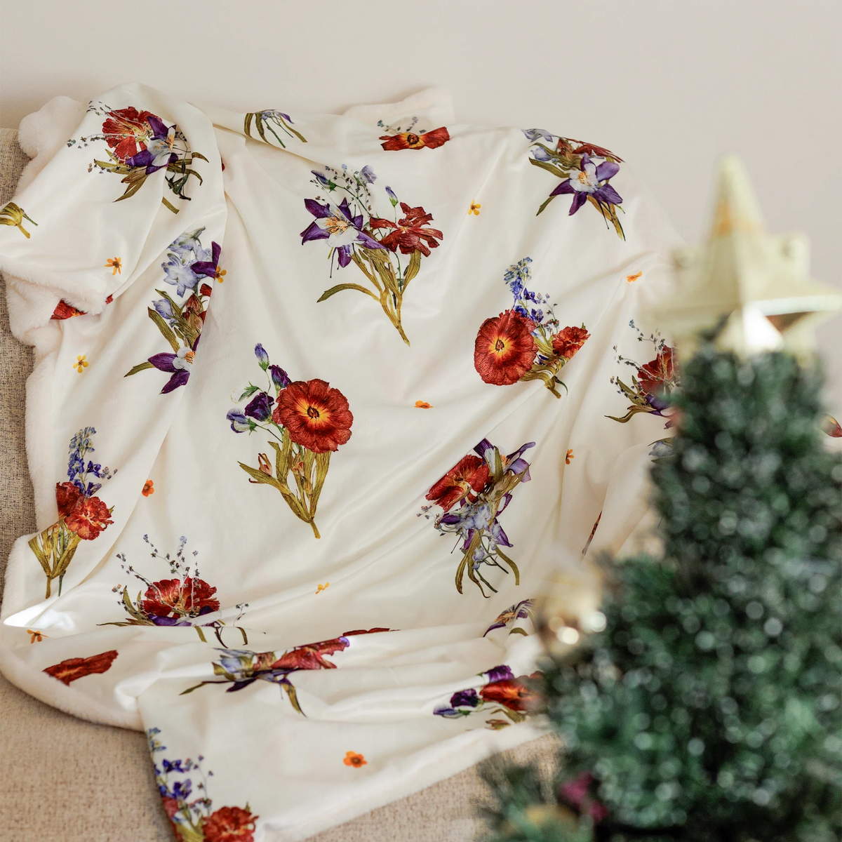 White blanket with bouquets of flowers design on a couch with a christmas tree in the foreground