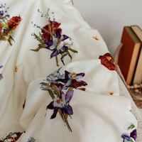 White blanket with antique themed pressed flower design and books in the background