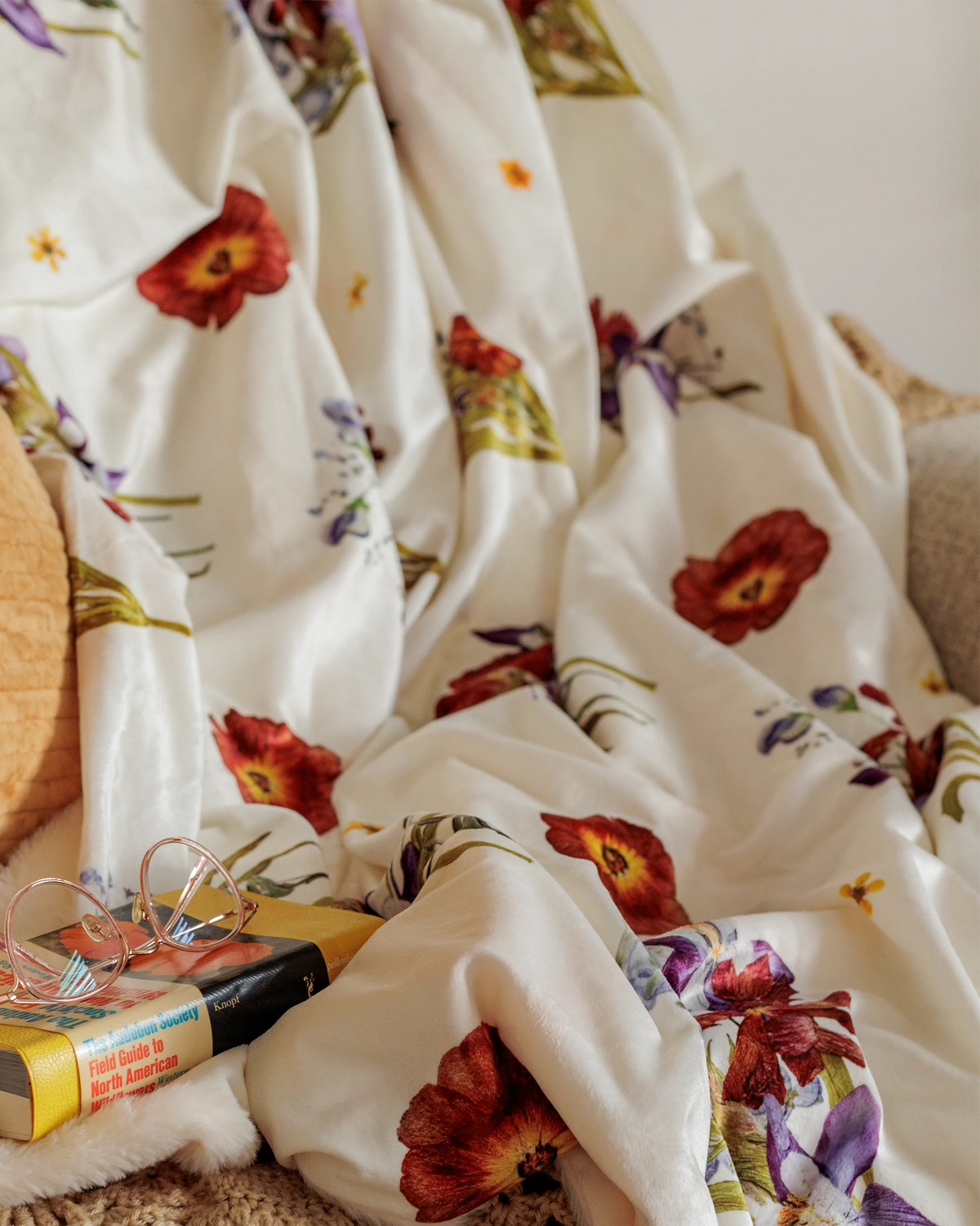 White throw blanket with pressed flower clusters print on a couch with a book and glasses in the foreground