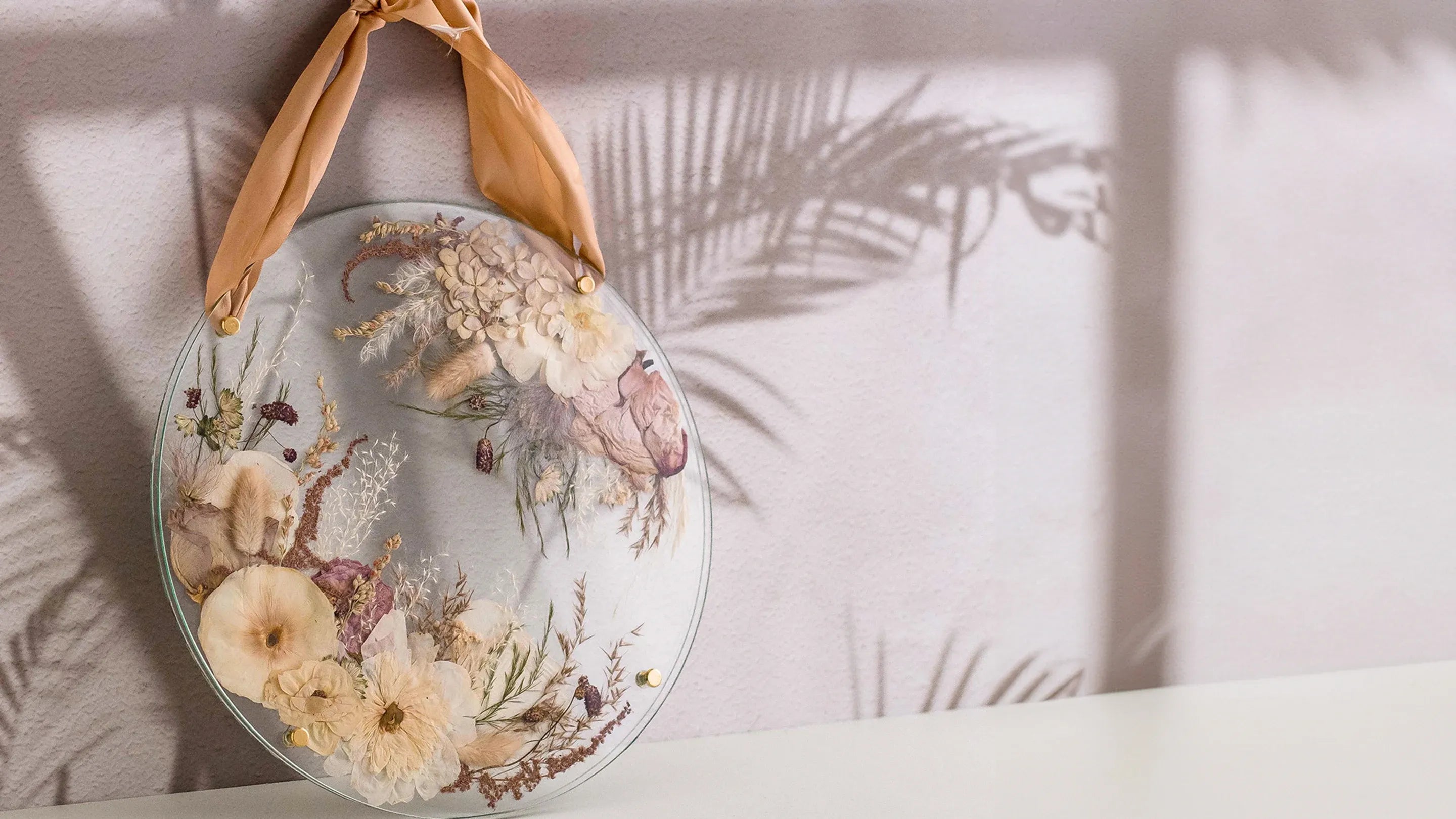 Unique pressed flower art in a circular bolted frame on a neutral background with shadows of foliage.