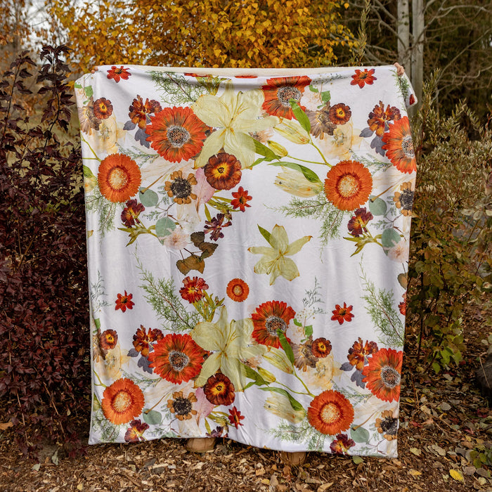 Floral-patterned blanket draped in a natural setting with trees and leaves.