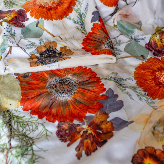 Floral and nature-themed throw blanket with orange flowers and green leaves.