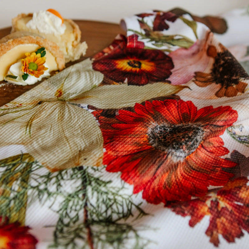 Pressed flower patterend fabric with a red flower on a wooden surface with pastries.