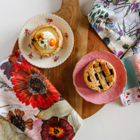 Two small pies on plates with decorative pressed flower tea towels
