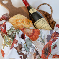 Wine bottle on a floral-patterned tea towel with bread and a basket in the background