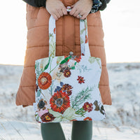 Person holding a floral tote bag with a blurred snowy background
