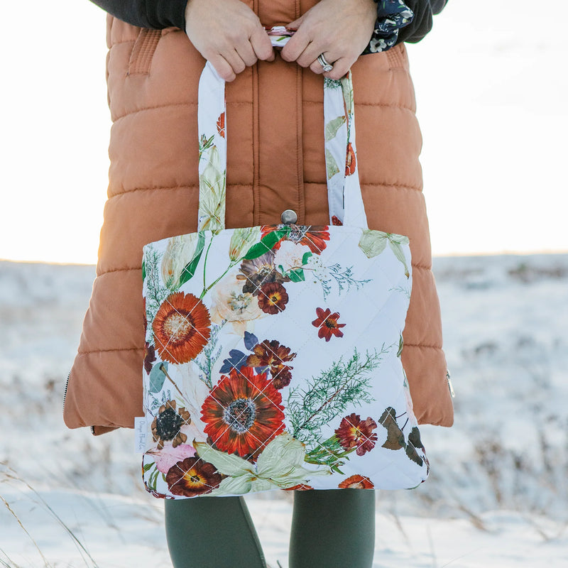 Person holding a floral tote bag with a blurred snowy background