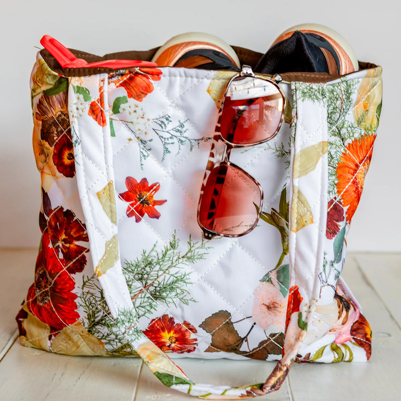 Floral-patterned tote bag with sunglasses and a hat on a white surface