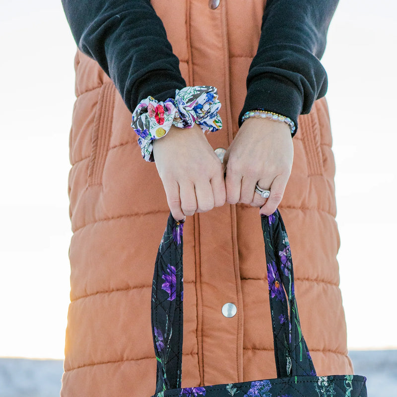 Person holding a bag handle outdoors with a floral scrunchie on their wrist