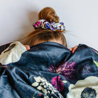 Woman playfully hiding behind a floral blanket with a bright matching floral scrunchie in her hair