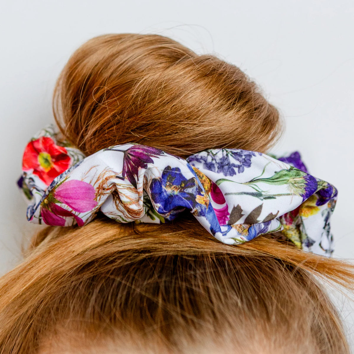 Colorful floral scrunchie on a bun against a white background