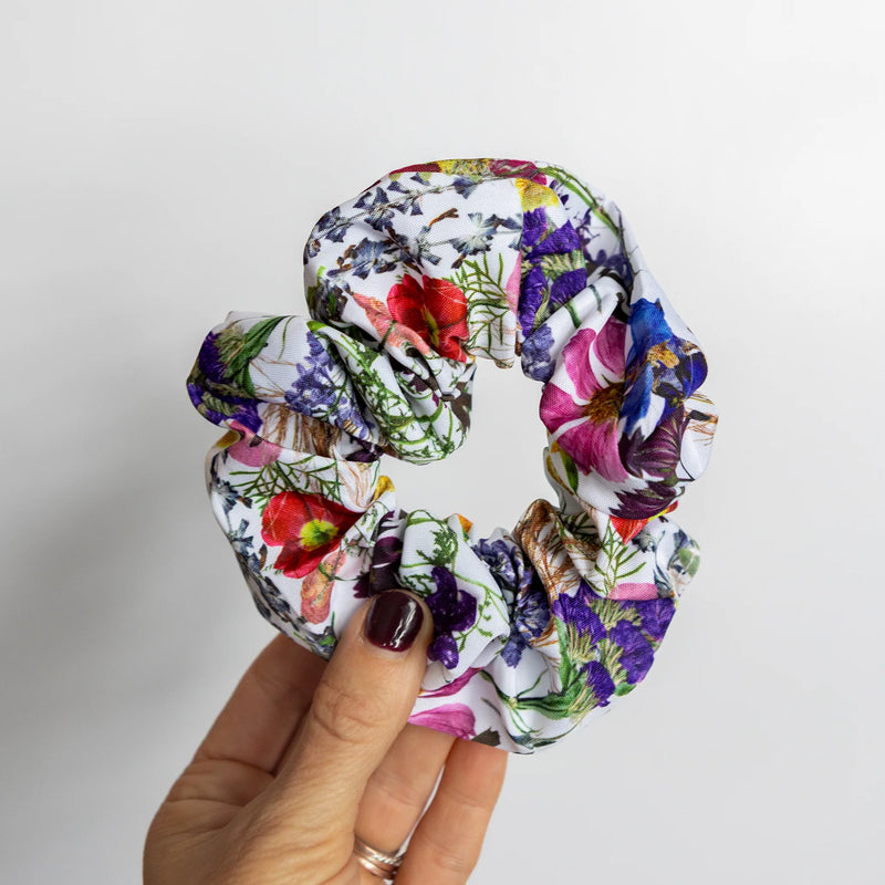 Hand holding a floral scrunchie against a plain background