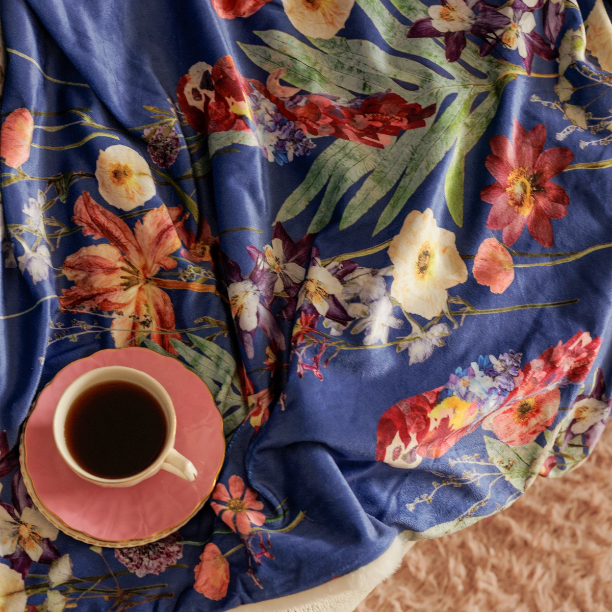 Tropical flower throw blanket with parrot design on a fluffy background with a tea cup on top