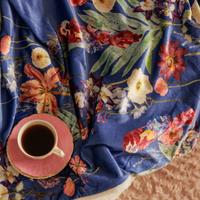 Tropical flower throw blanket with parrot design on a fluffy background with a tea cup on top