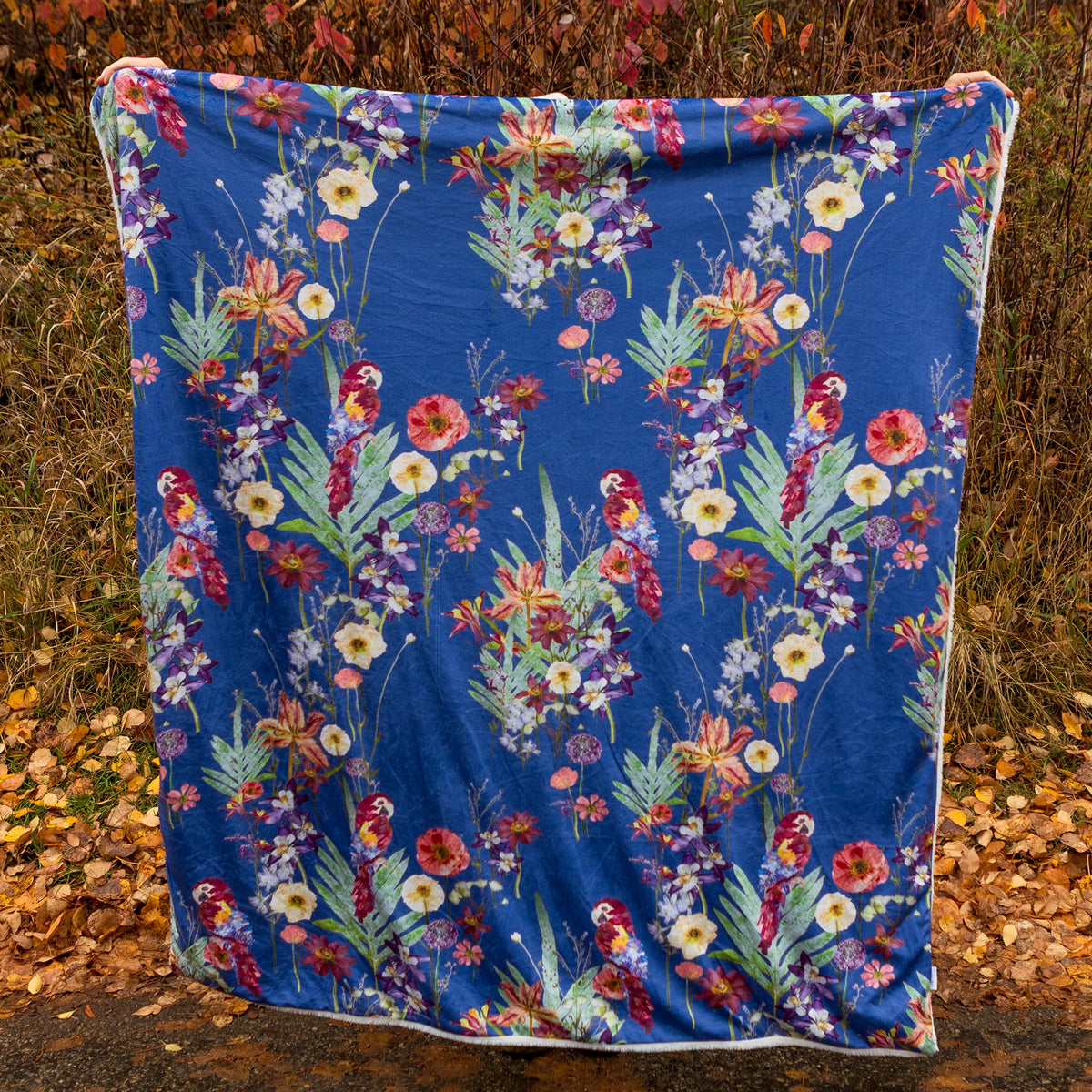 Blue tropical blanket with parrots and flowers being held up in an autumn scene outdoors