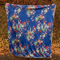 Blue tropical blanket with parrots and flowers being held up in an autumn scene outdoors