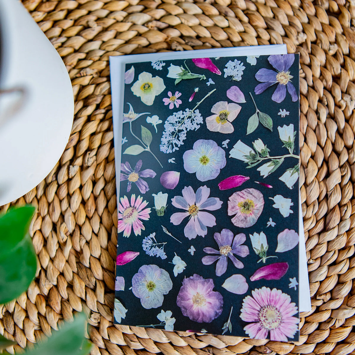 Greeting card with black background dotted with pastel coloured flowers on a woven surface