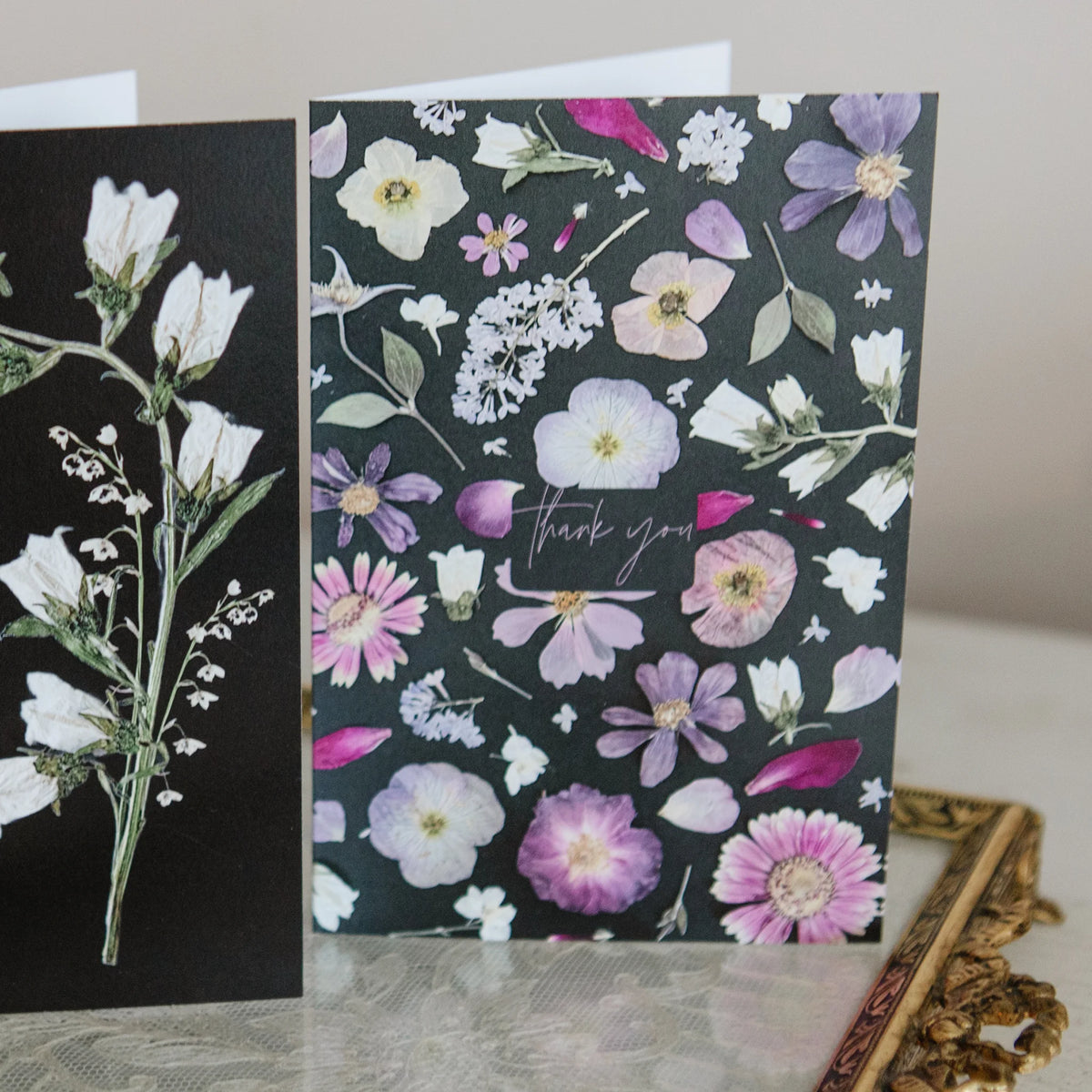 Floral-patterned card with 'thank you' text on a dark background, next to a card with white flowers on a black background.