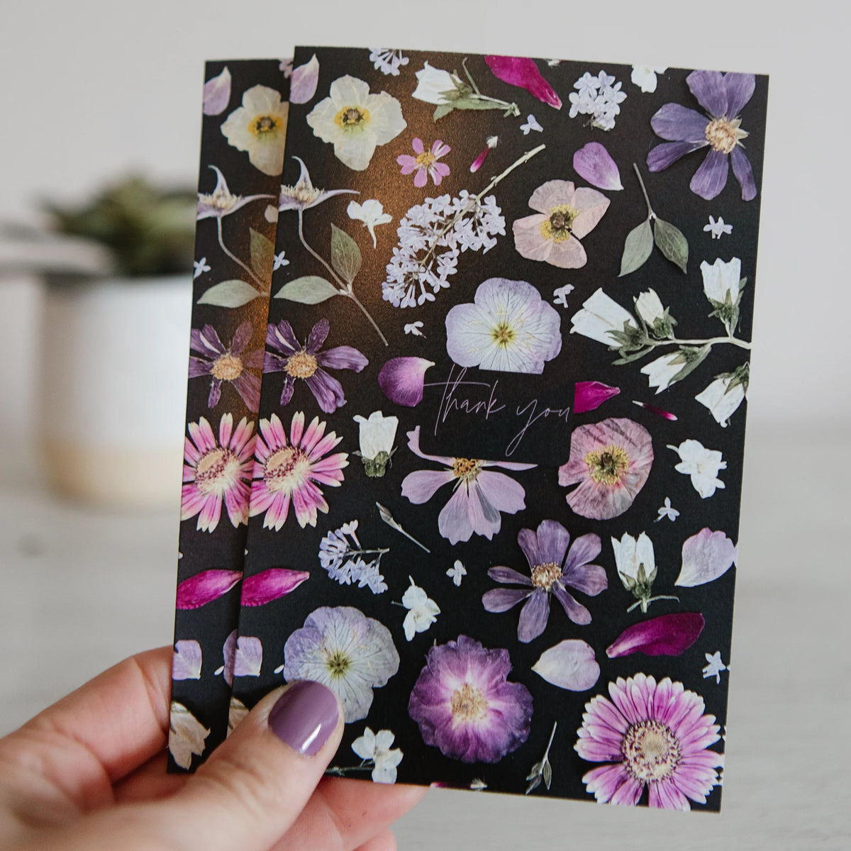 Floral-patterned cards with 'thank you' text held by a hand against a neutral background