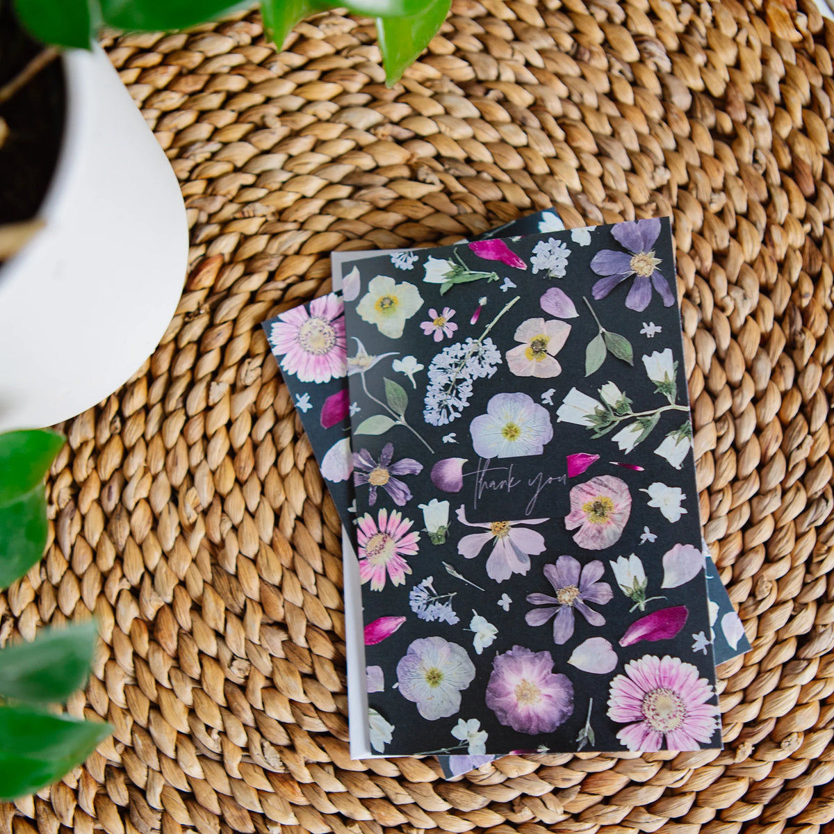 Floral-patterned greeting card on a woven surface with a plant in the corner