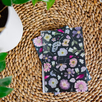 Floral-patterned greeting card on a woven surface with a plant in the corner