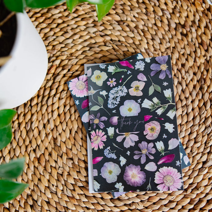 Floral-patterned greeting card on a woven surface with a plant in the corner