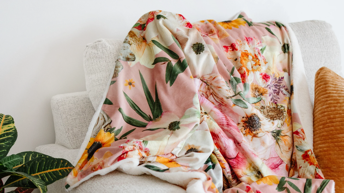 Peaches & Sunshine floral throw blanket draped over a cozy grey couch