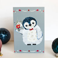 Card with a penguin design holding flowers on a gray background