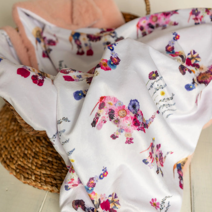 Floral and elephant-patterned baby blanket draped over a wicker basket.