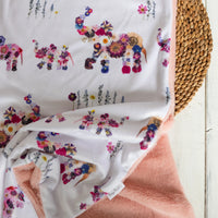 Floral-patterned baby blanket draped over a woven basket on a wooden surface