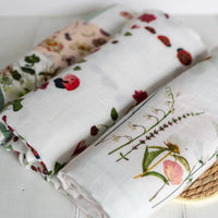 Folded fabric swaddles with floral and nature-themed prints on a light wooden surface.