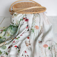Floral-patterned muslin swaddles draped over a wicker basket on a white surface