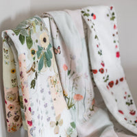 Three floral-patterned baby swaddles hanging against a neutral background