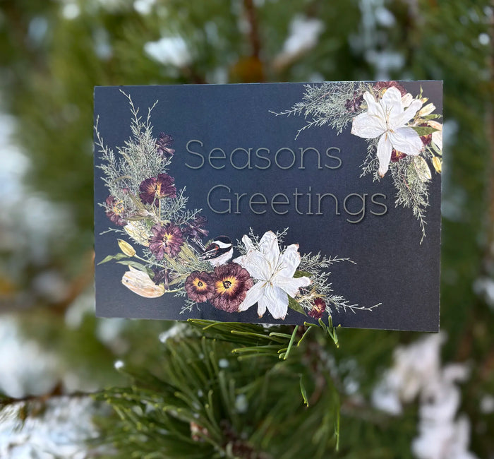 Seasons Greetings card with floral design on a snowy tree background
